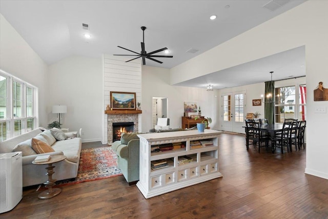 living area with lofted ceiling, a large fireplace, ceiling fan with notable chandelier, french doors, and dark wood-style floors