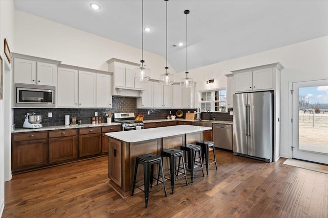 kitchen featuring a breakfast bar area, stainless steel appliances, dark wood-style flooring, a kitchen island, and light countertops