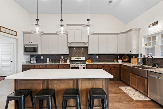 kitchen with vaulted ceiling, appliances with stainless steel finishes, wood finished floors, and a kitchen bar