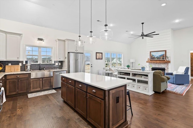 kitchen with a fireplace, stainless steel appliances, light countertops, open floor plan, and a sink