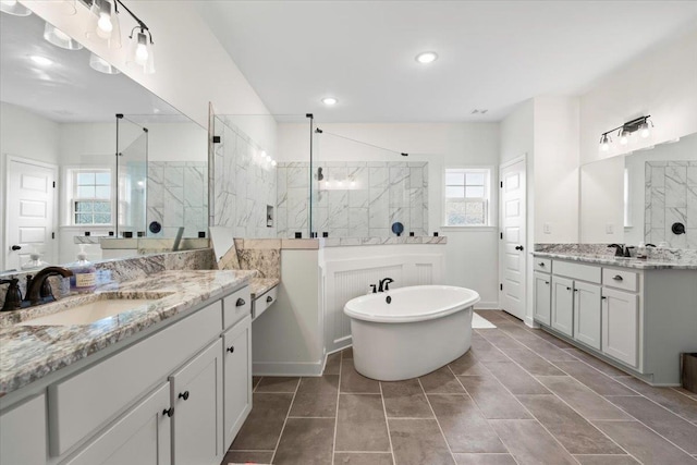 bathroom with a walk in shower, two vanities, a soaking tub, and a sink