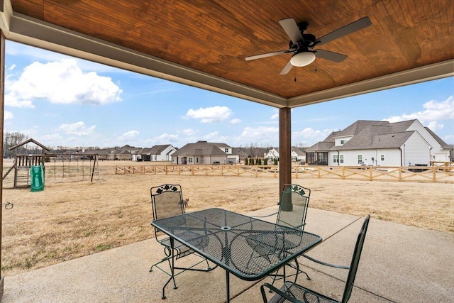 view of patio featuring ceiling fan, outdoor dining area, a playground, a fenced backyard, and a residential view