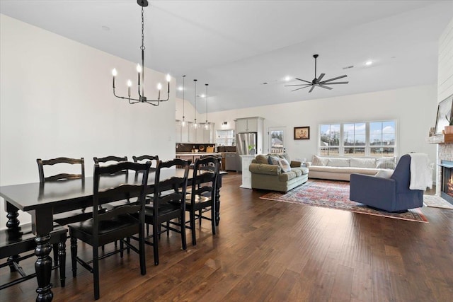 dining space with recessed lighting, ceiling fan with notable chandelier, dark wood-style flooring, a towering ceiling, and a lit fireplace