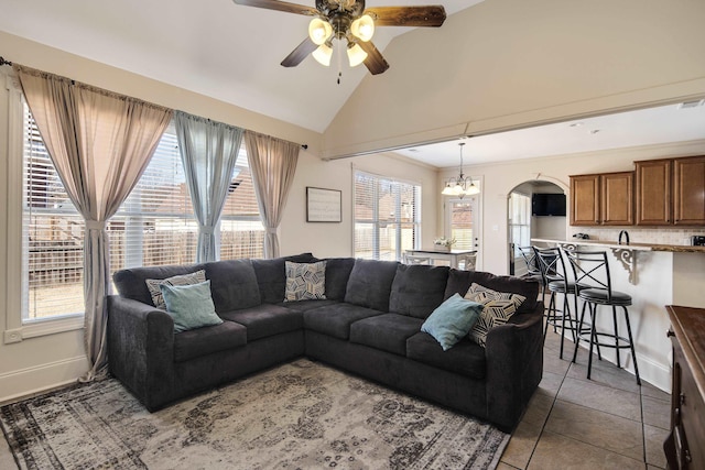 tiled living room featuring lofted ceiling, a healthy amount of sunlight, and ceiling fan with notable chandelier