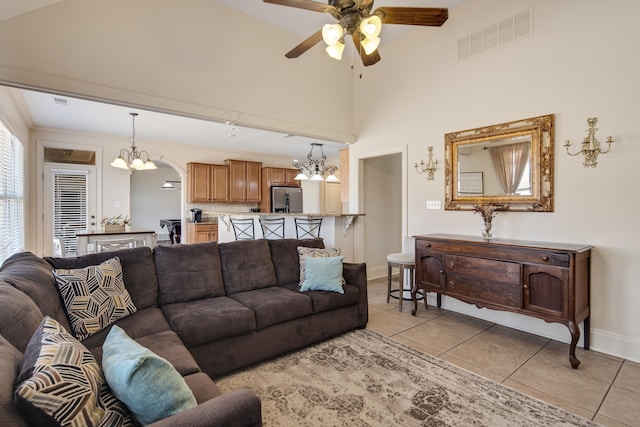 living area with light tile patterned floors, visible vents, high vaulted ceiling, baseboards, and ceiling fan with notable chandelier