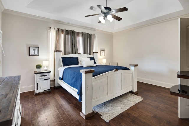 bedroom with a tray ceiling, dark wood-style flooring, visible vents, and baseboards