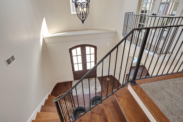 stairway with arched walkways, wood finished floors, visible vents, baseboards, and french doors