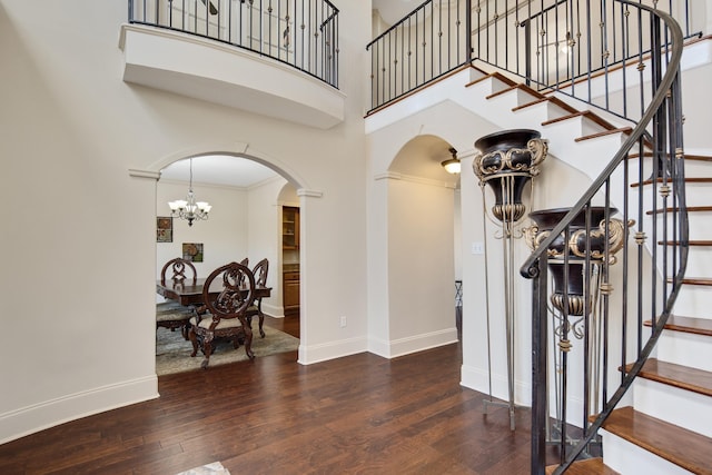 foyer with arched walkways, an inviting chandelier, wood finished floors, and baseboards