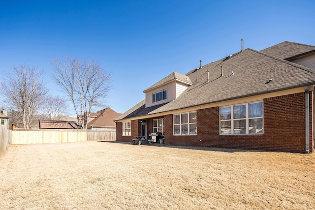 back of house featuring brick siding, a patio, a shingled roof, a lawn, and a fenced backyard