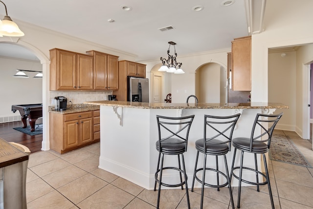 kitchen featuring arched walkways, a kitchen bar, stainless steel fridge, and visible vents