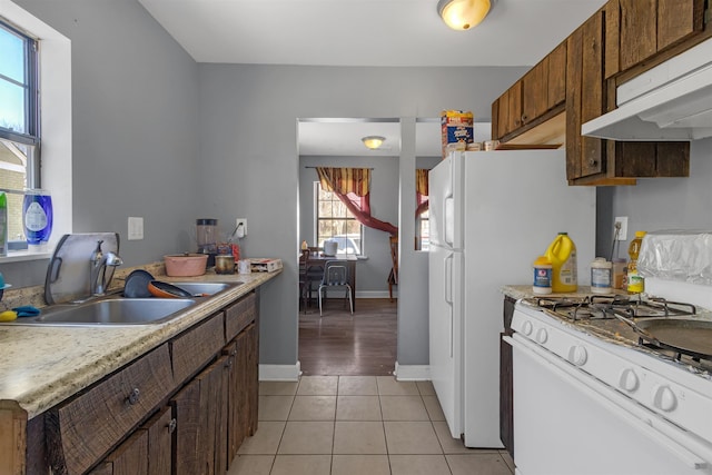 kitchen with light tile patterned floors, white gas range oven, light countertops, under cabinet range hood, and a sink