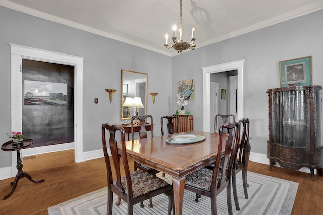 dining space with baseboards, visible vents, ornamental molding, wood finished floors, and a chandelier