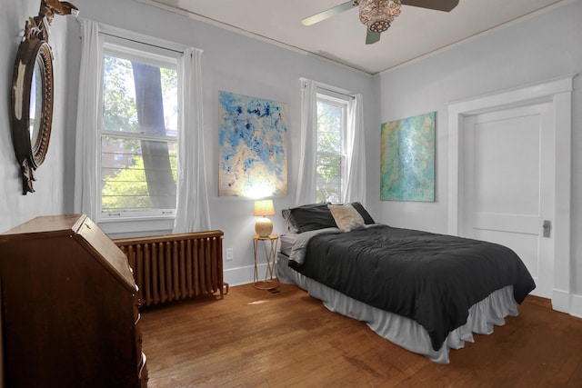 bedroom featuring multiple windows, radiator heating unit, wood finished floors, and baseboards