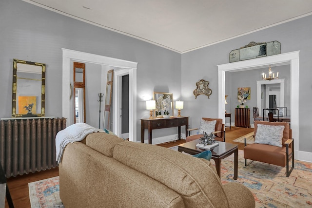 living room with wood finished floors, baseboards, radiator, an inviting chandelier, and crown molding