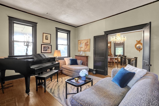 living area featuring an inviting chandelier, wood-type flooring, ornamental molding, and a textured ceiling