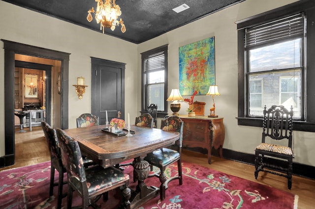 dining area with baseboards, wood finished floors, visible vents, and an inviting chandelier