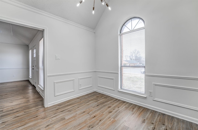 unfurnished room with wainscoting, wood finished floors, vaulted ceiling, crown molding, and a decorative wall