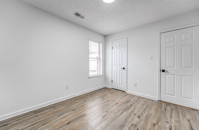 spare room featuring a textured ceiling, wood finished floors, visible vents, and baseboards