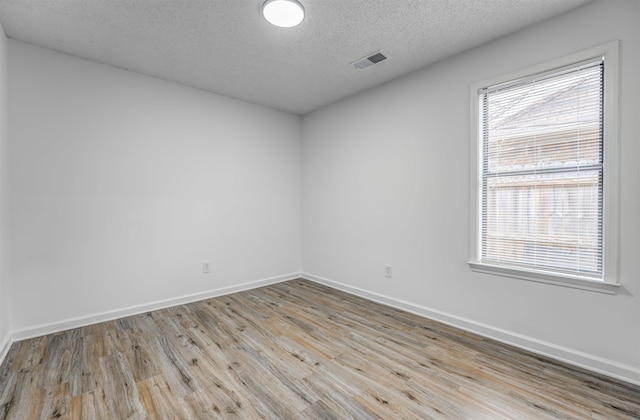 unfurnished room with a healthy amount of sunlight, a textured ceiling, visible vents, and wood finished floors