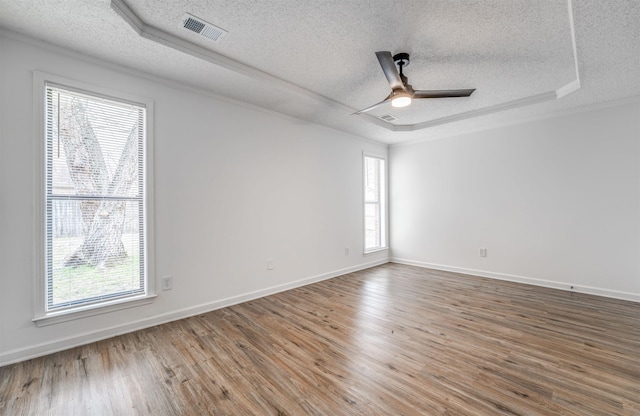 empty room with a textured ceiling, wood finished floors, visible vents, a ceiling fan, and a tray ceiling