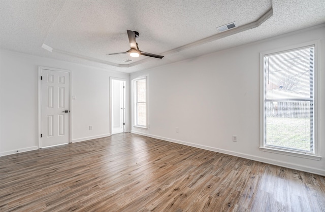 empty room with wood finished floors, a raised ceiling, visible vents, and a healthy amount of sunlight