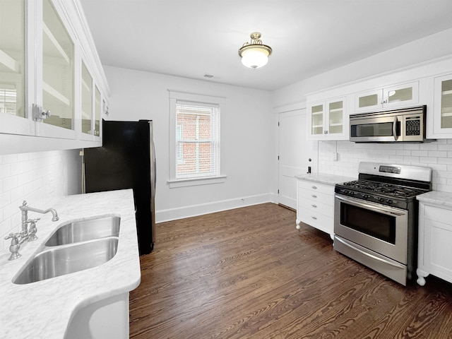 kitchen with dark wood-style floors, decorative backsplash, appliances with stainless steel finishes, a sink, and light stone countertops