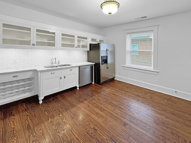 kitchen with stainless steel appliances, dark wood-style flooring, a sink, tasteful backsplash, and glass insert cabinets