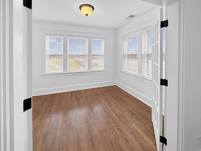 empty room with dark wood-style flooring, visible vents, and baseboards