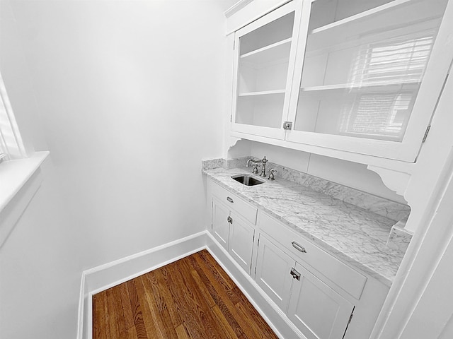 bar with dark wood-style flooring, a sink, and baseboards