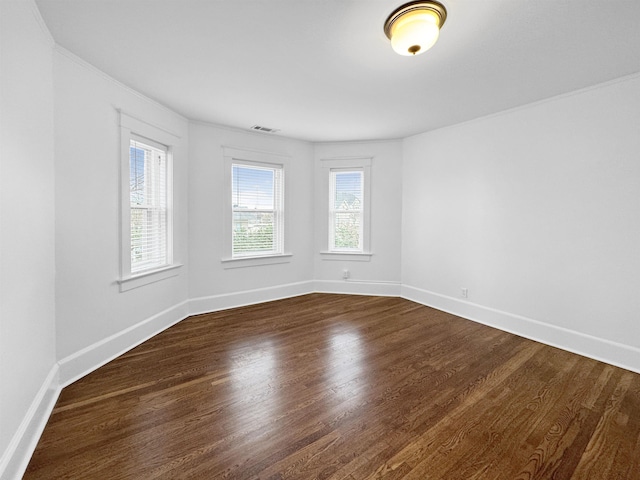 empty room with dark wood-style floors, visible vents, and baseboards