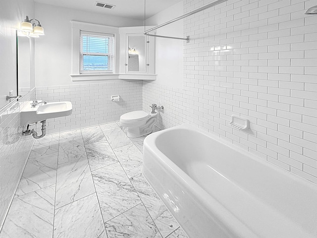 bathroom featuring visible vents, tile walls, toilet, marble finish floor, and a sink