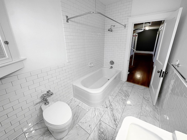 bathroom featuring toilet, marble finish floor, tile walls, and shower / bathtub combination