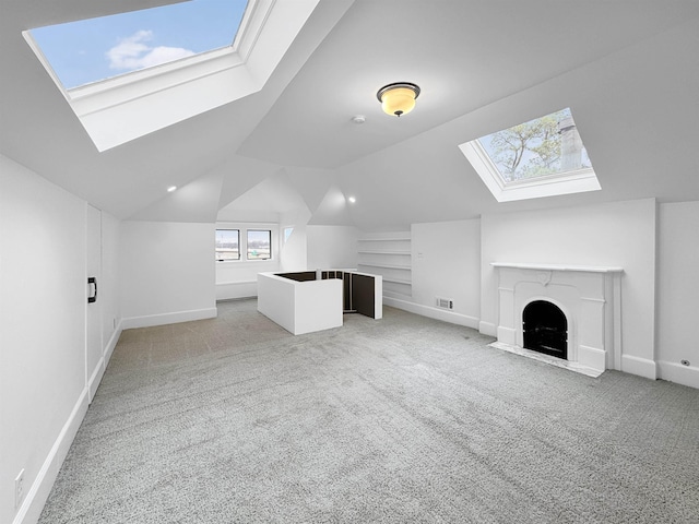 additional living space featuring light carpet, vaulted ceiling with skylight, a fireplace with flush hearth, and built in shelves