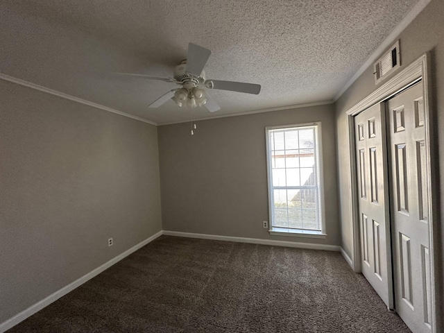 unfurnished bedroom with a textured ceiling, visible vents, baseboards, ornamental molding, and dark colored carpet