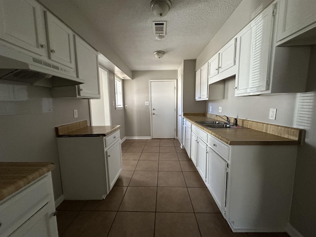 kitchen with under cabinet range hood, visible vents, white cabinets, and a sink