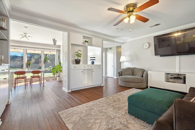 living room featuring dark wood-style floors, visible vents, a ceiling fan, and ornamental molding