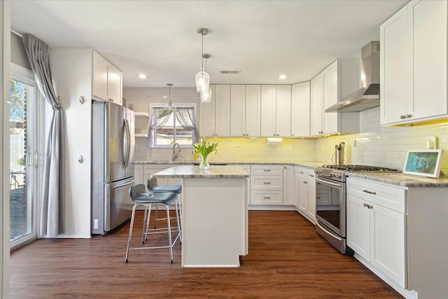 kitchen with stainless steel appliances, dark wood-type flooring, white cabinets, a center island, and wall chimney exhaust hood