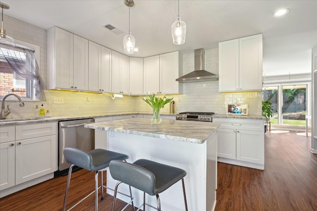 kitchen with visible vents, dark wood-style floors, wall chimney exhaust hood, stainless steel appliances, and a sink