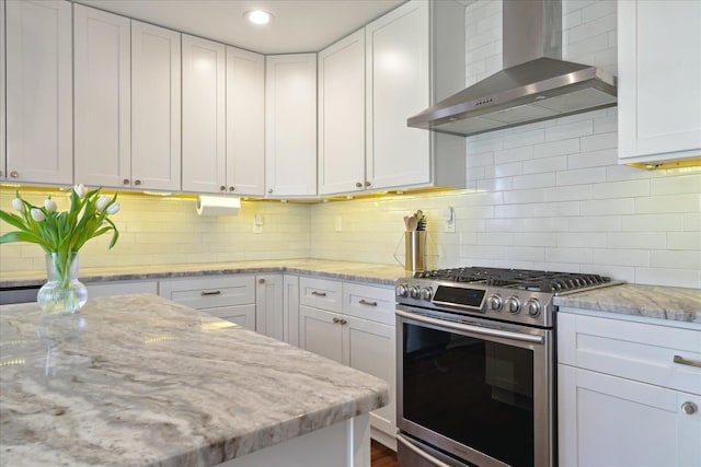 kitchen featuring light stone counters, white cabinets, wall chimney range hood, and gas range