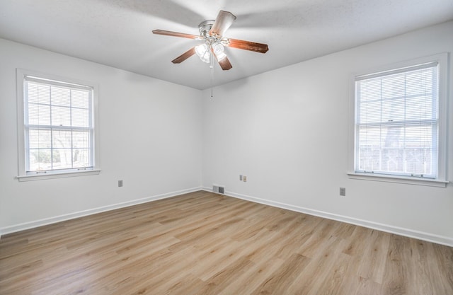 unfurnished room featuring a healthy amount of sunlight, visible vents, baseboards, and wood finished floors