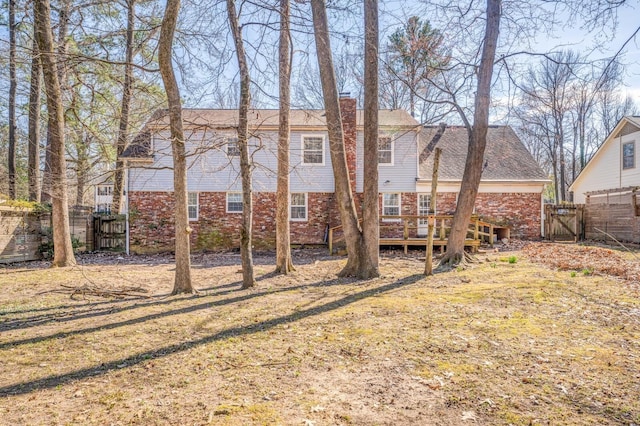 rear view of property with a wooden deck, brick siding, fence, and a gate