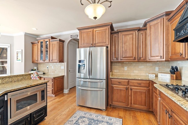 kitchen featuring appliances with stainless steel finishes, light wood-type flooring, brown cabinetry, and crown molding