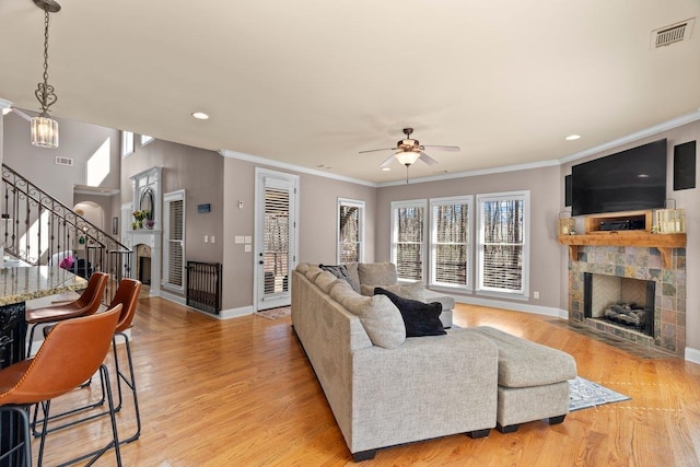 living area with a tile fireplace, light wood-style flooring, visible vents, baseboards, and stairs