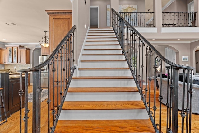 stairs with crown molding, visible vents, arched walkways, and wood finished floors