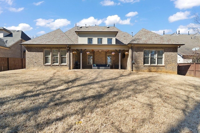 rear view of property featuring brick siding, a yard, roof with shingles, a patio area, and fence