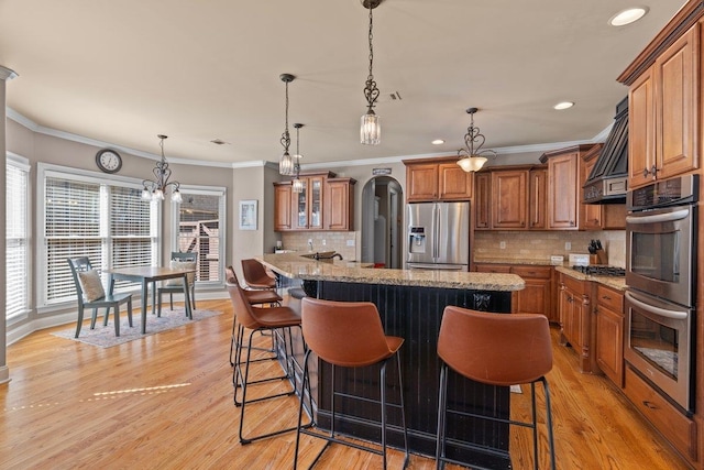 kitchen featuring light stone counters, a breakfast bar area, appliances with stainless steel finishes, light wood-type flooring, and brown cabinetry