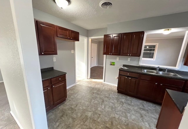 kitchen with baseboards, visible vents, dark countertops, a textured ceiling, and a sink