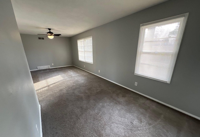 unfurnished room with dark colored carpet, visible vents, ceiling fan, and baseboards