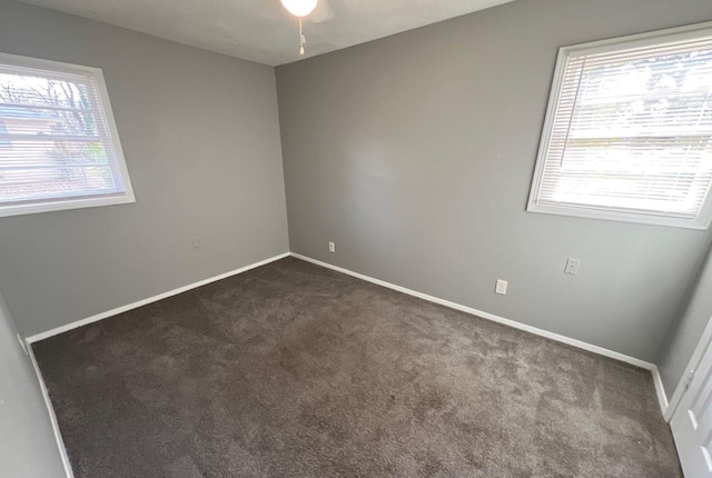 spare room featuring plenty of natural light, baseboards, and dark colored carpet