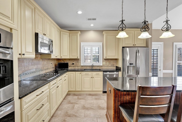 kitchen with visible vents, dark stone countertops, stainless steel appliances, cream cabinetry, and a sink